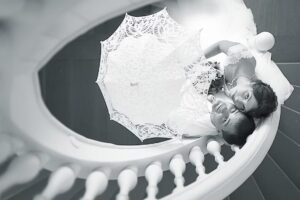 Bride and groom lying on a staircase holding a lace umbrella at a private event space St. Louis, romantic wedding portrait in black and white.