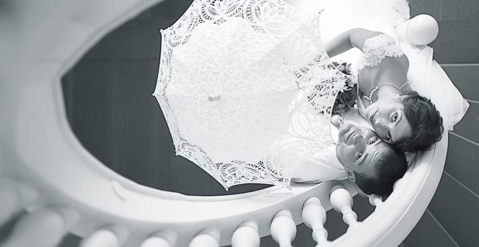 Bride and groom lying on a staircase holding a lace umbrella at a private event space St. Louis, romantic wedding portrait in black and white.
